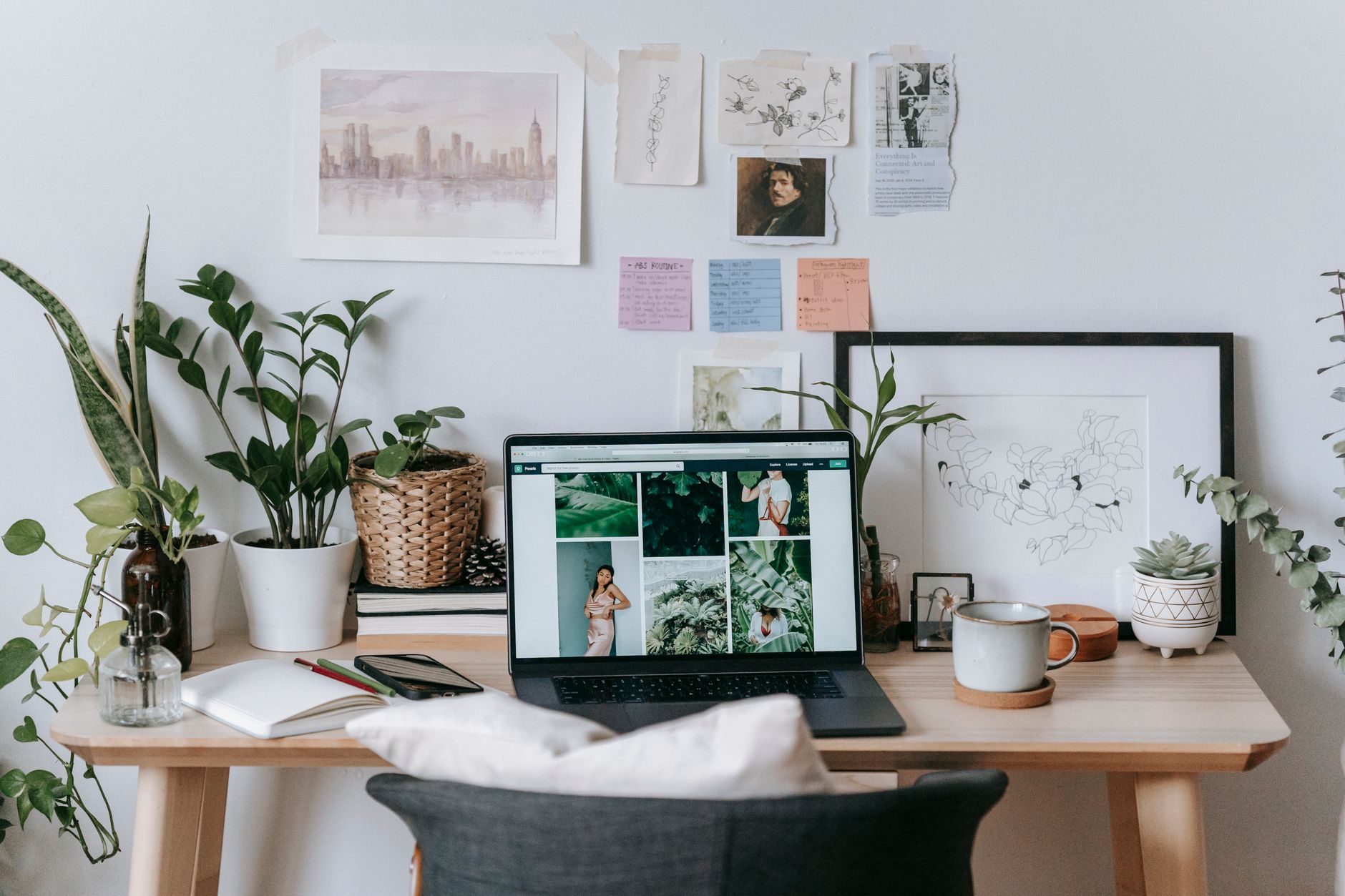 Bureau à domicile en bois clair avec un ordinateur portable, un smartphone et un carnet ouvert, entouré de plantes vertes